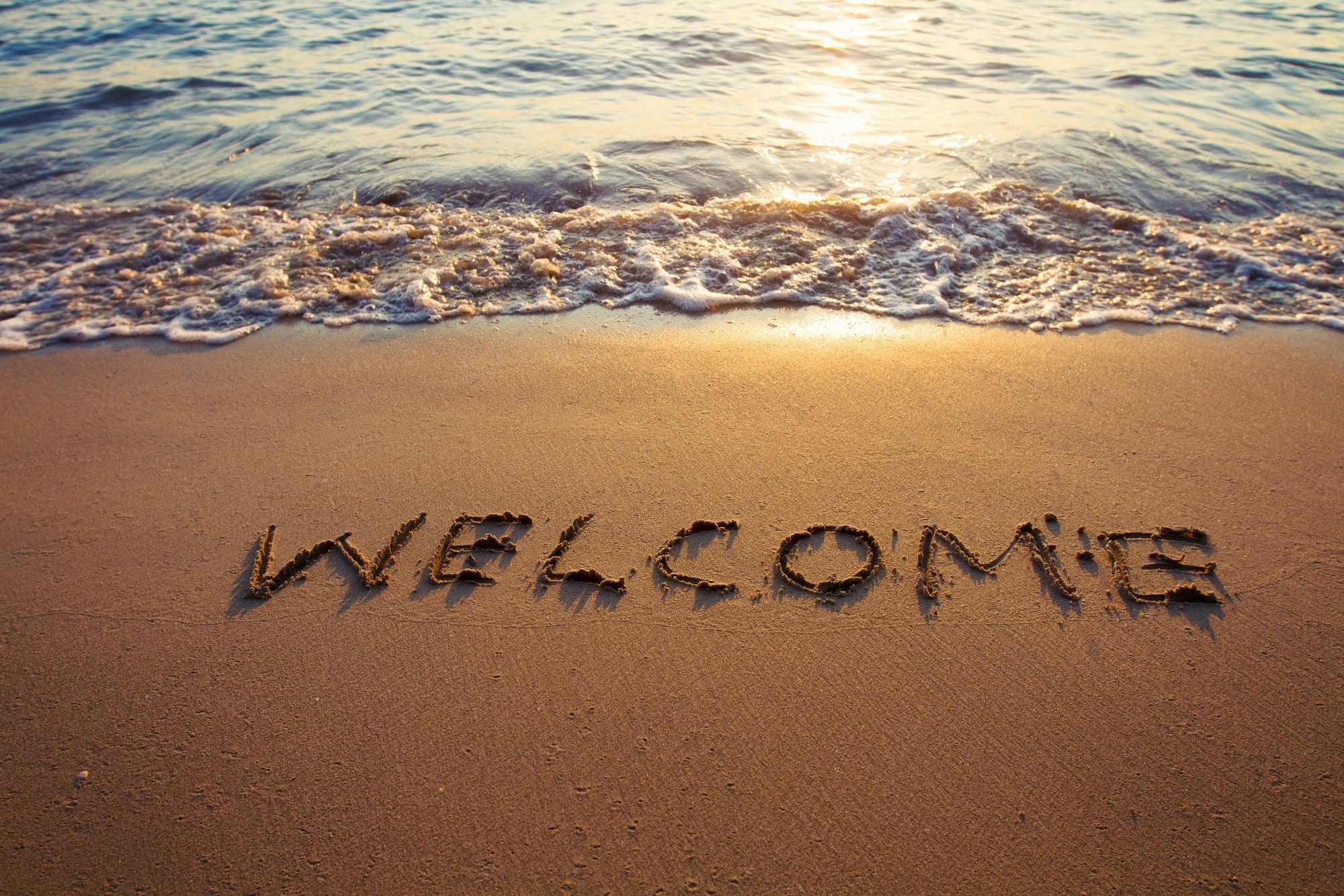 The word "Welcome" written in the sand on a golden sandy beach